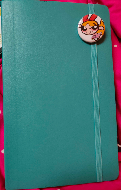 Teal Moleskine notebook with a round button of Blossom from the Powerpuff Girls on the elastic band.